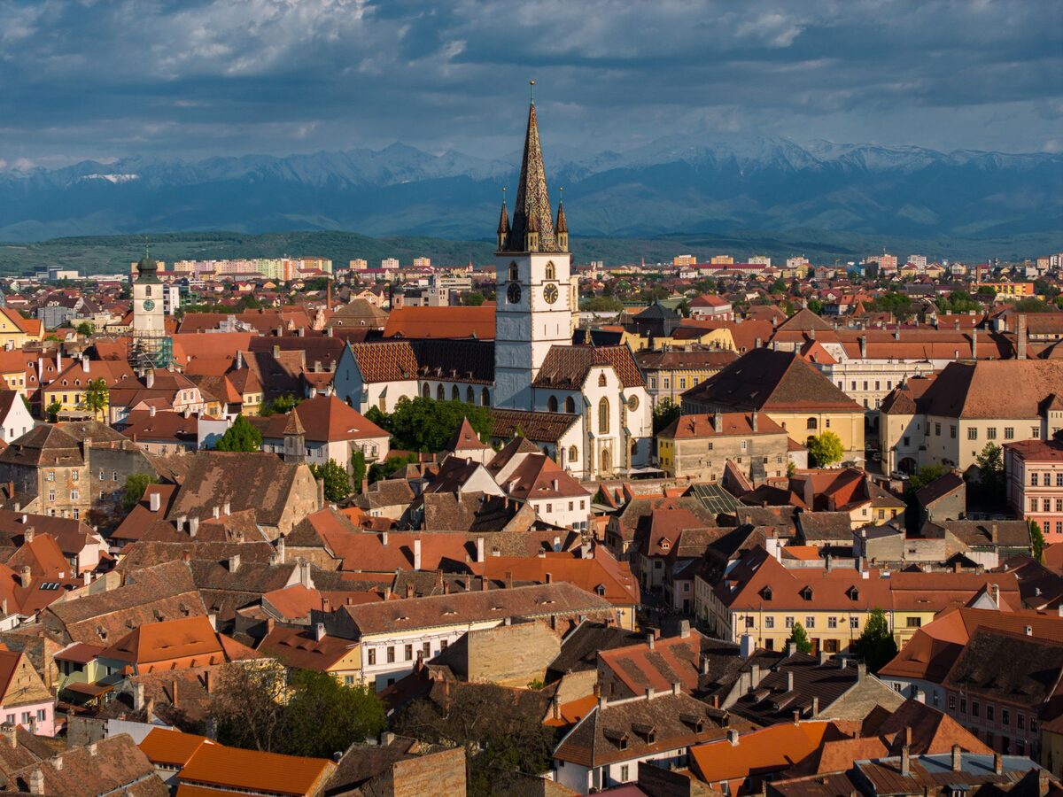 The Lutheran Cathedral's tall spire rising above Sibiu's red rooftops, with snow-capped mountains behind