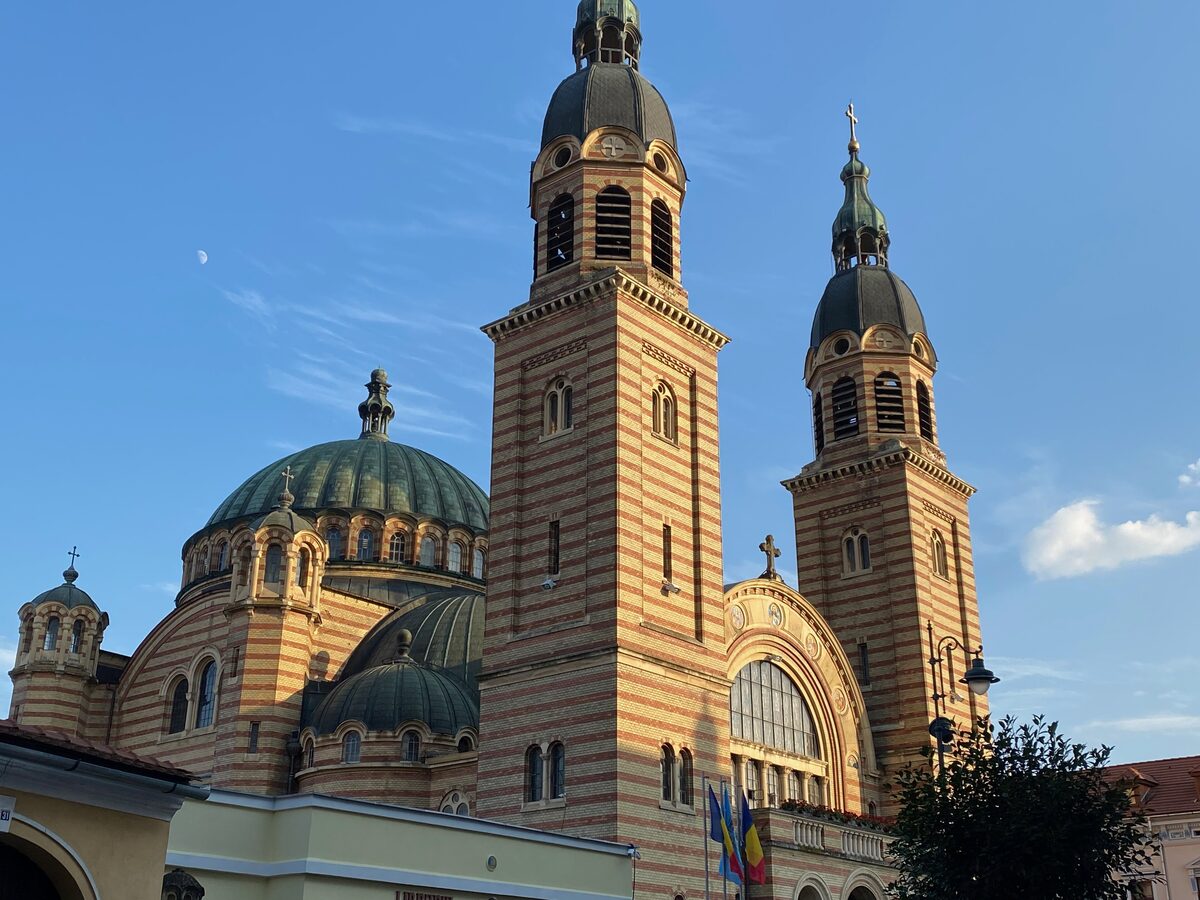 The striped brick-and-stone towers and green domes of Sibiu's Holy Trinity Orthodox Cathedral against a blue sky