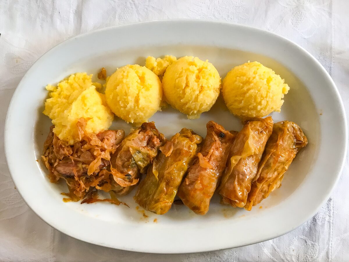 Sarmale cabbage rolls with a side of sauerkraut and four scoops of yellow polenta on a white plate