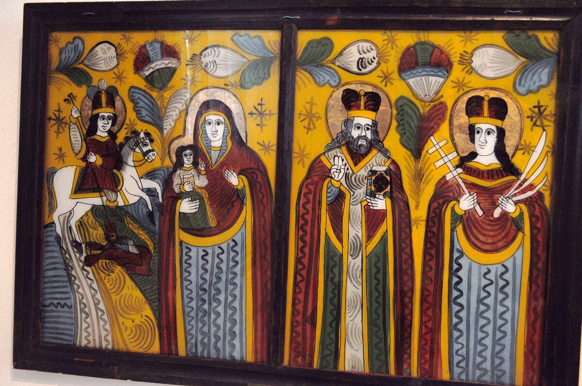 Two folk icons painted on glass in the Sibiel museum: St. George on a white horse, and the Virgin and Child with two crowned saints on a bright yellow background