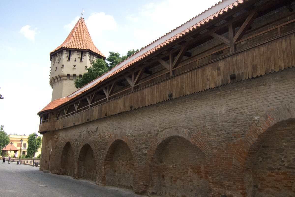 The brick town wall on Strada Cetății, with arched niches and a roofed wooden walkway, leading to a tower with a red tiled roof