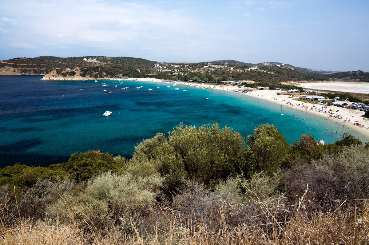 The long curve of Golden Beach on Ammouliani, turquoise water and boats in the bay below a scrubby hillside