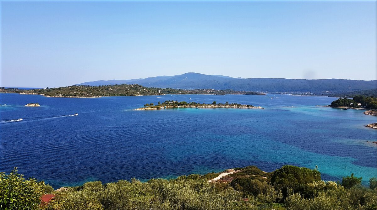 Blue water between small islands and wooded headlands, seen from a viewpoint above the coast