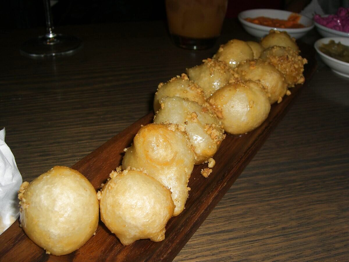 A row of fried loukoumades sprinkled with crushed walnuts on a wooden board