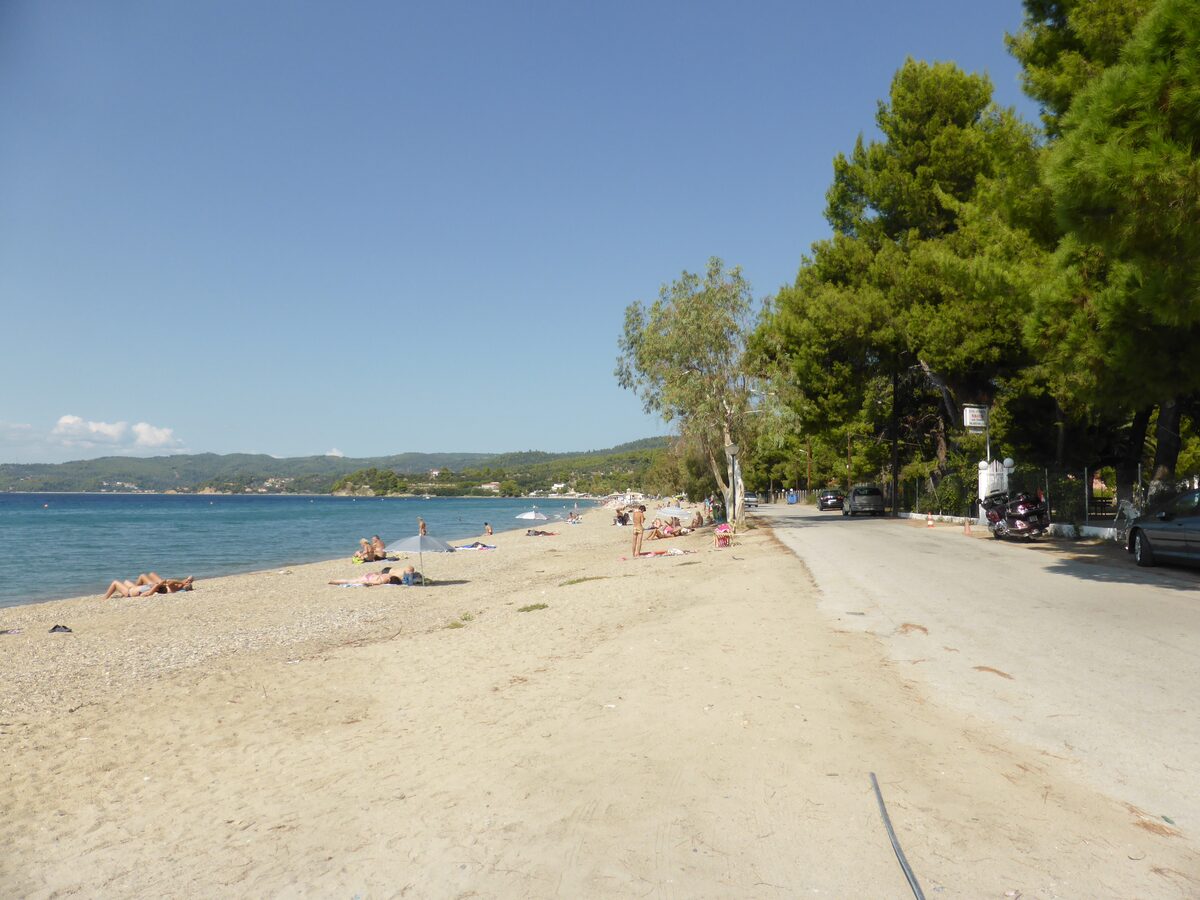Paradisos beach just outside Neos Marmaras on a sunny day: pale sand, calm blue sea, pines and a road behind the beach, and a few sunbathers