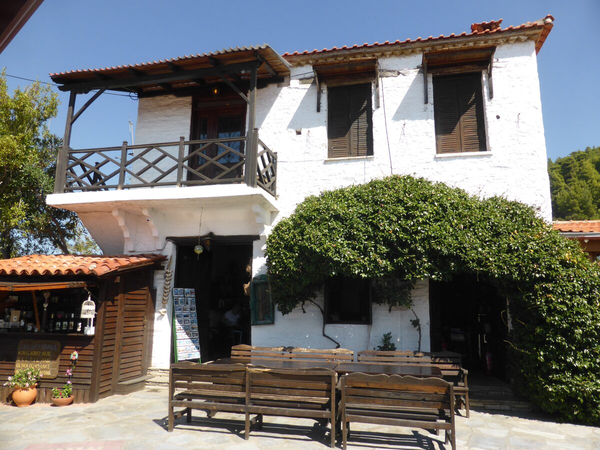 A whitewashed taverna in Parthenonas with a wooden balcony, a vine-covered arch and long wooden benches outside