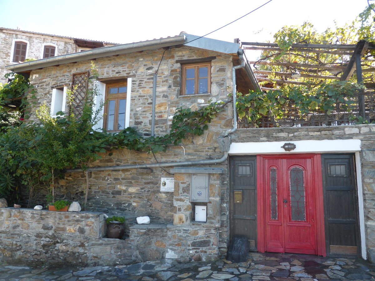 A restored stone house in Parthenonas, with a red front door, a vine-covered terrace and a cobbled lane