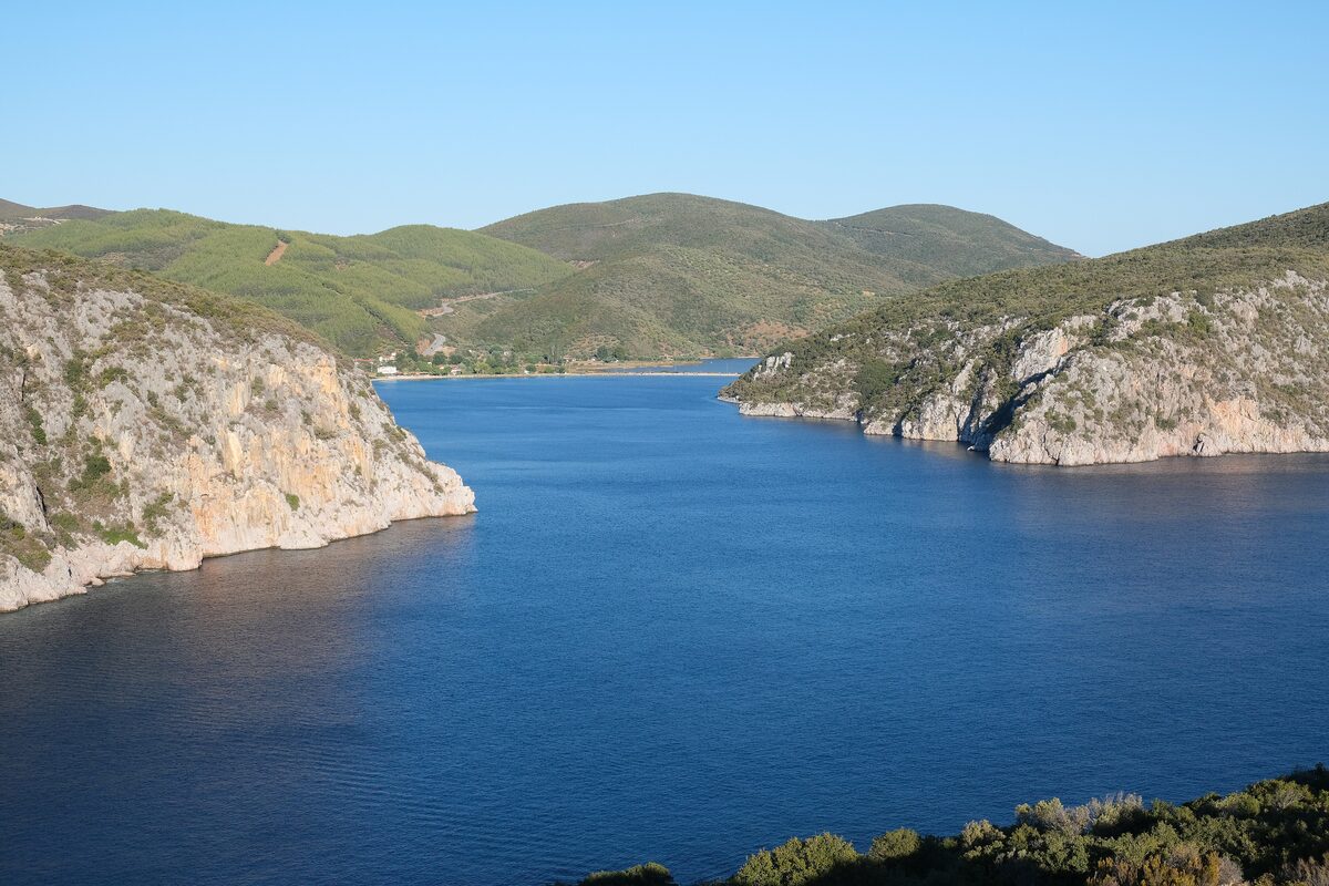 Deep blue water between rocky cliffs at the entrance to the Porto Koufo bay, with green hills beyond