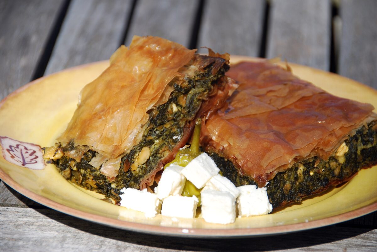 A slice of spinach pie in flaky filo, with cubes of feta on a yellow plate