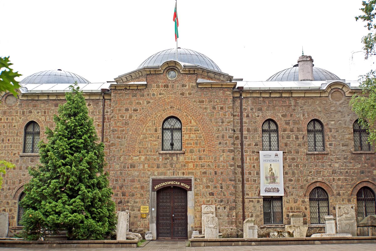 The stone-and-brick facade of the former Grand Mosque, now the National Archaeological Museum, with its lead domes, Bulgarian flag and ancient stone slabs lined up along the wall.