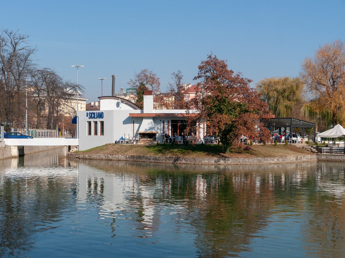 Lake Ariana in Borisova Gradina in autumn, with a lakeside cafe and red and golden trees reflected in the still water.