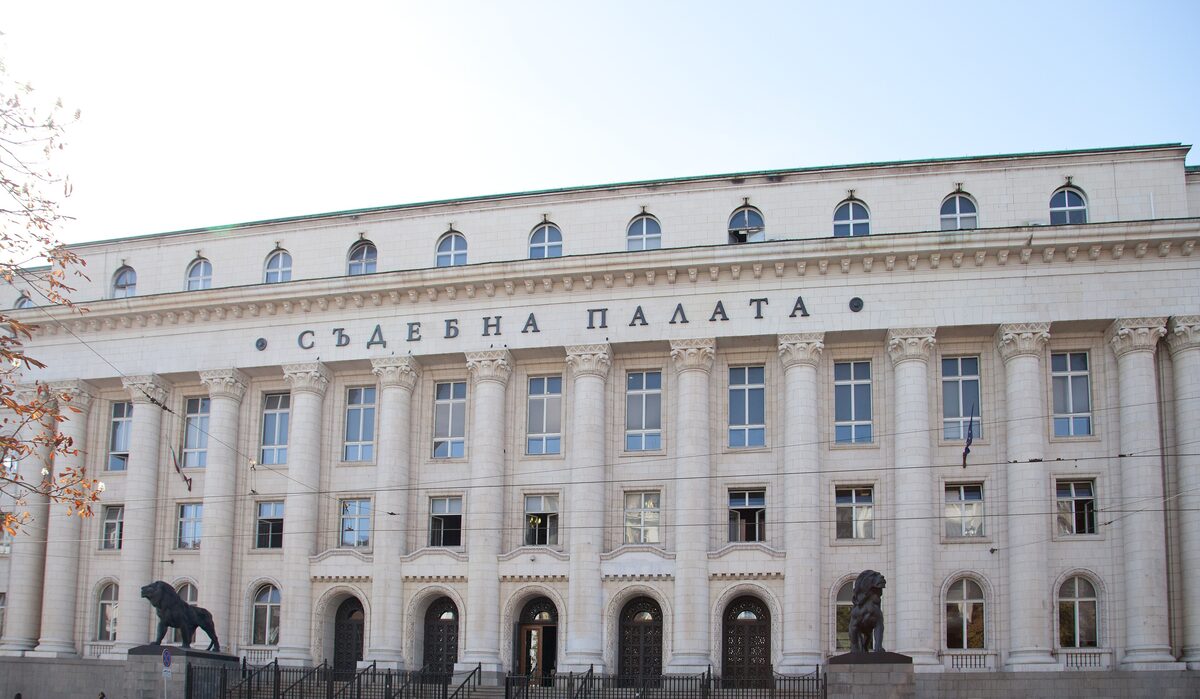 The long colonnaded facade of the Palace of Justice with 'Съдебна палата' over the columns and a bronze lion on each side of the entrance.