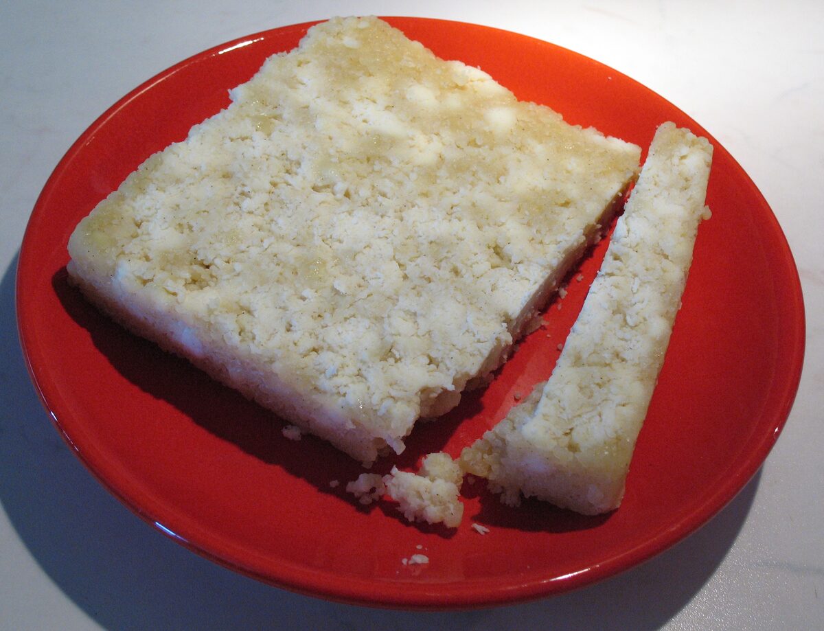 A slab and a cut strip of Tyrolean Graukäse on a red plate, pale and crumbly