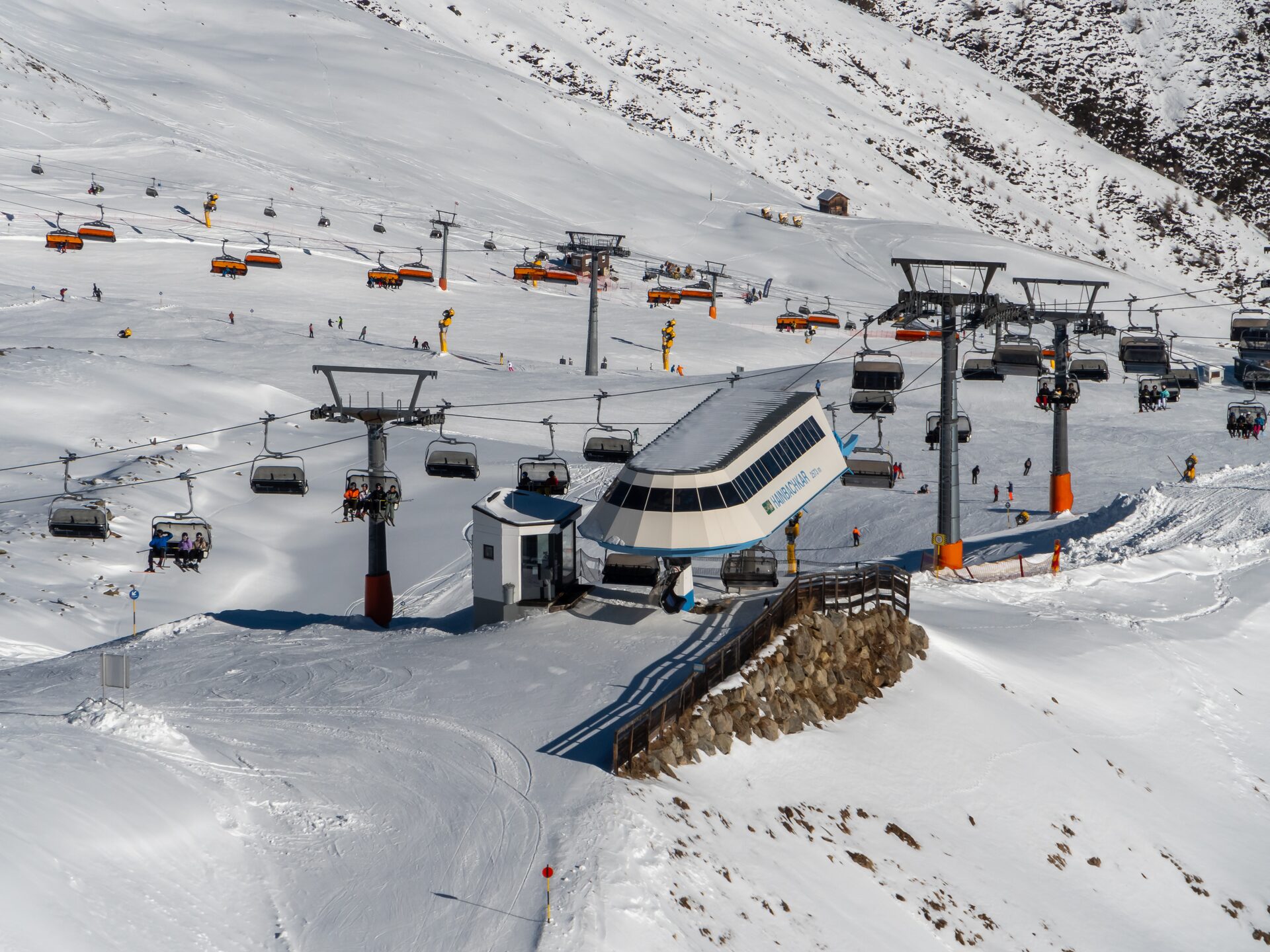 The Hainbachkar chairlift station in Sölden, with orange chairs and skiers on the snowy pistes around it