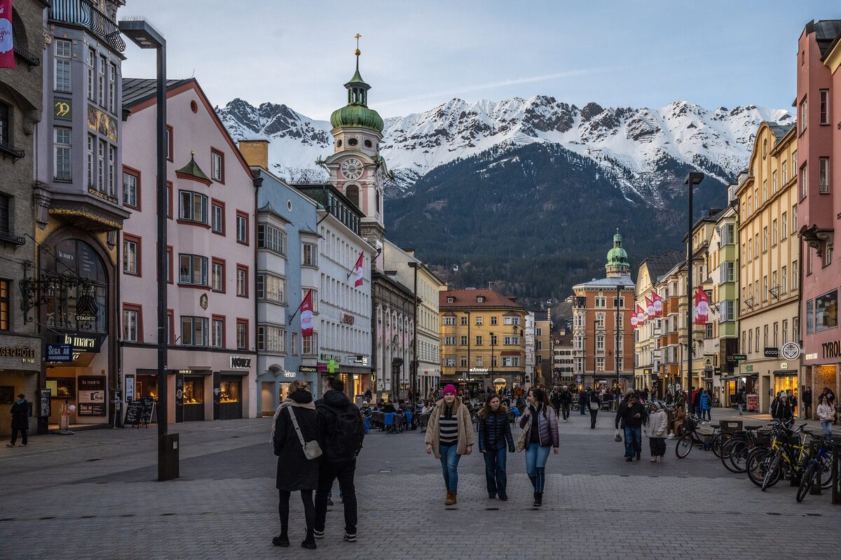 Maria-Theresien-Strasse in Innsbruck in the evening, with the Spitalskirche tower and the snow-covered Nordkette range rising behind the old town