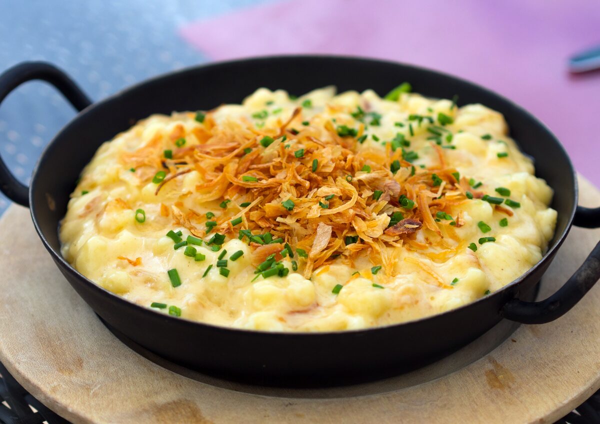 Cheese spaetzle in a black pan, topped with crispy fried onions and chives