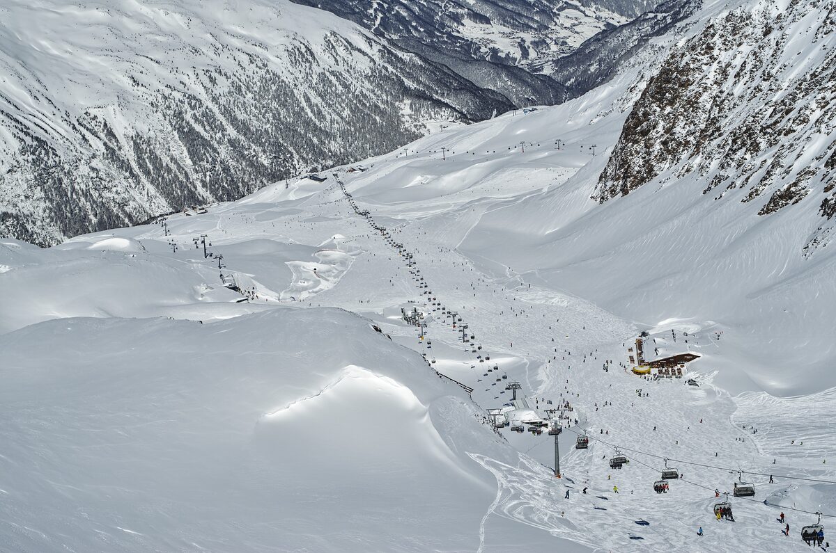 Chairlifts running up a wide snowy bowl in the Obergurgl-Hochgurgl ski area, with skiers spread across the slopes