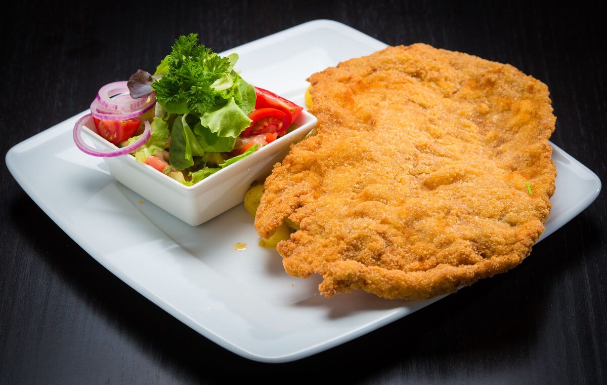 A golden breaded schnitzel next to a small salad on a white plate