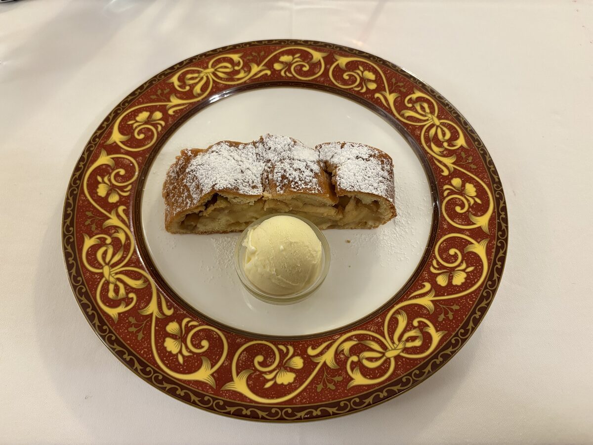 A slice of apple strudel dusted with sugar, served with a scoop of ice cream