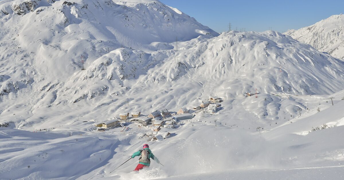 A skier in fresh powder on a steep slope above St. Christoph am Arlberg, with the village in the valley below
