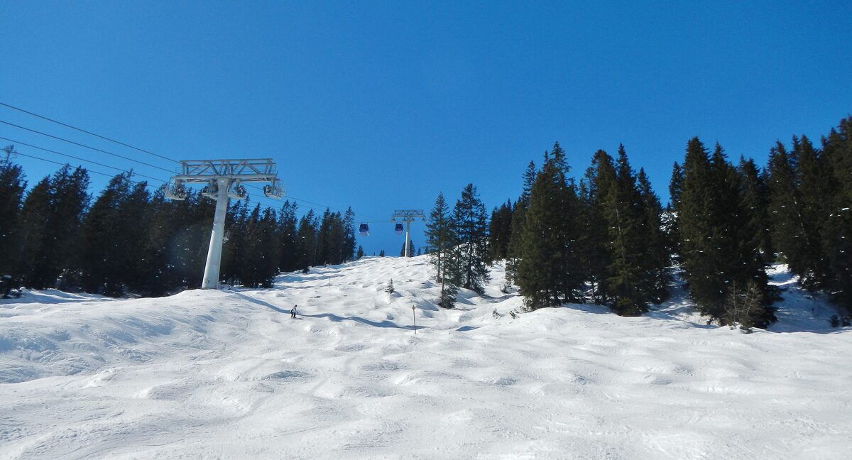 A piste in fresh snow below a chairlift on the Galzig, with pines and a blue sky