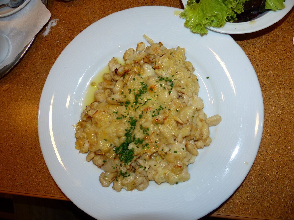 Käsespätzle, cheese noodles topped with fried onion and fresh herbs on a white plate
