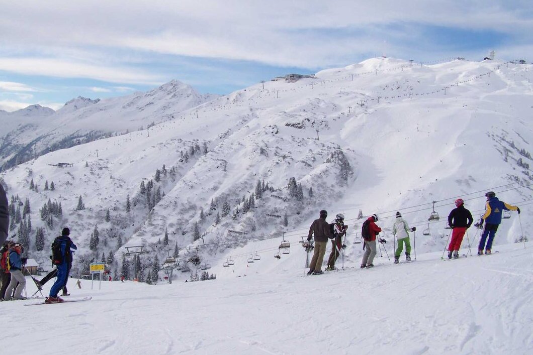 Skiers lined up on a slope at Gampen above St. Anton, with a chairlift and the snowy Galzig mountain behind