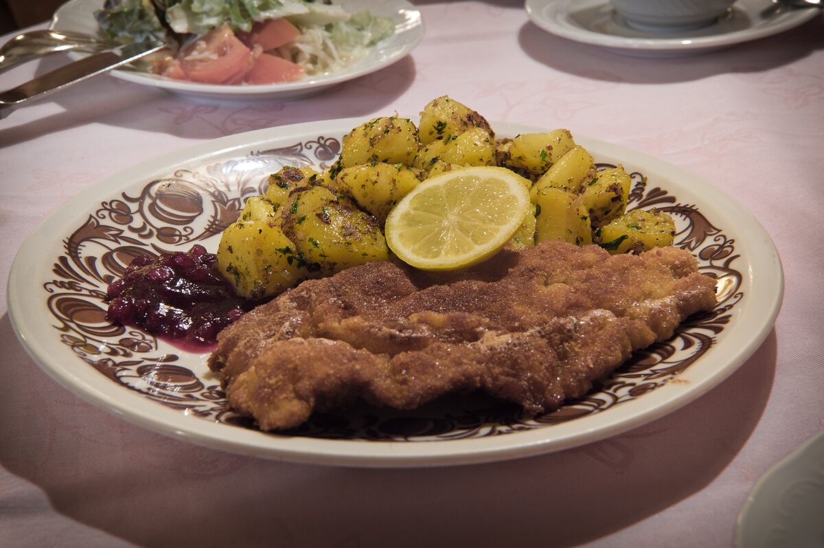 A breaded Wiener Schnitzel with boiled potatoes, a lemon wedge and cranberry jam