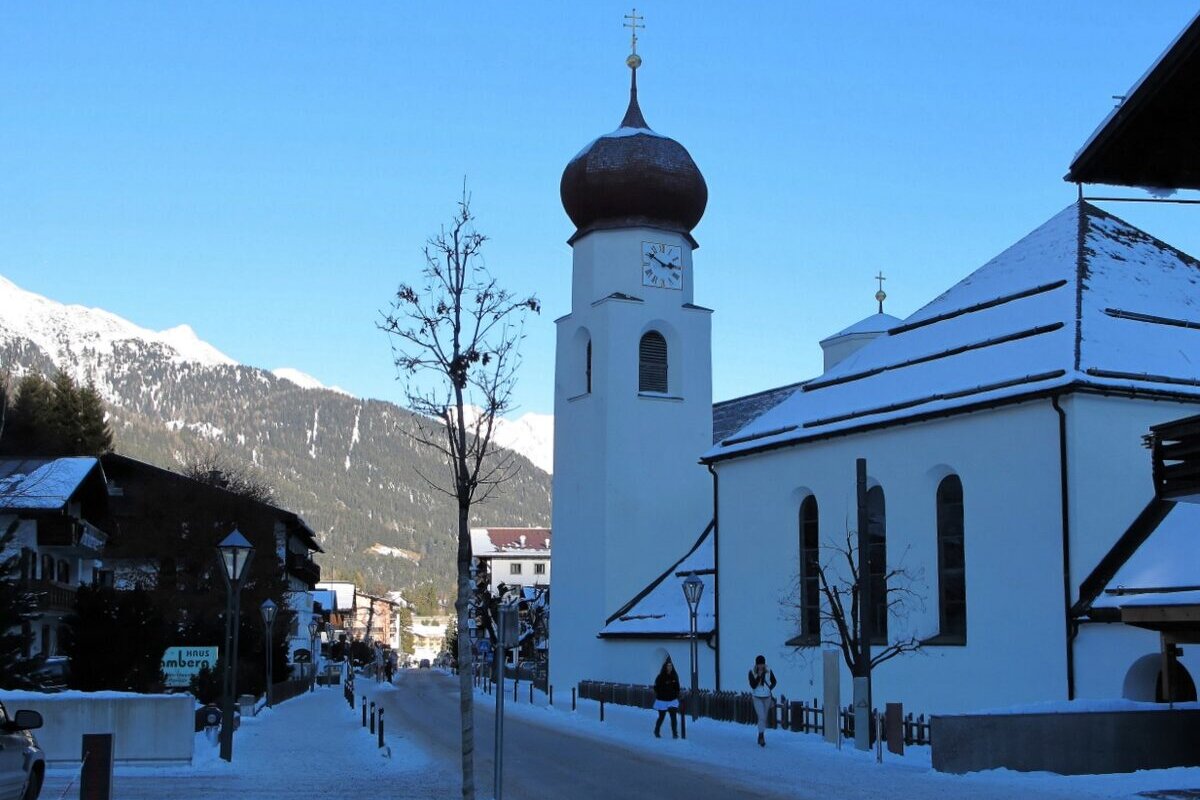 The white parish church of St. Anton with its onion dome on a snowy village street, under a blue winter sky