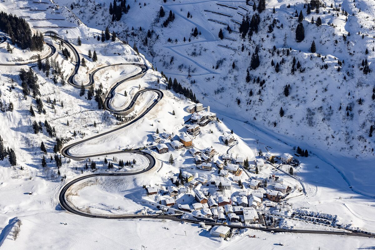 Stuben in deep snow from above, with the hairpin bends of the Arlberg road climbing the slope beside the village