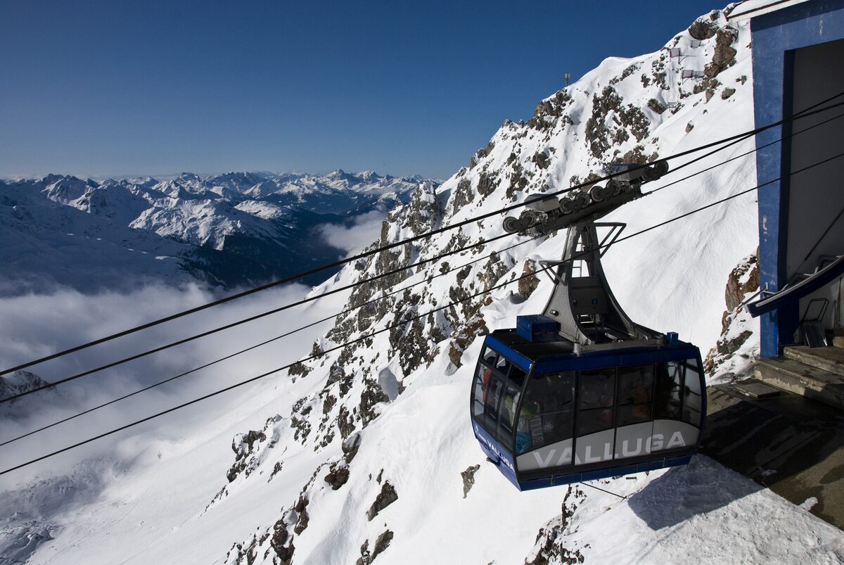 The top station of the Valluga cable car in snow, with a cabin arriving and snowy mountains behind