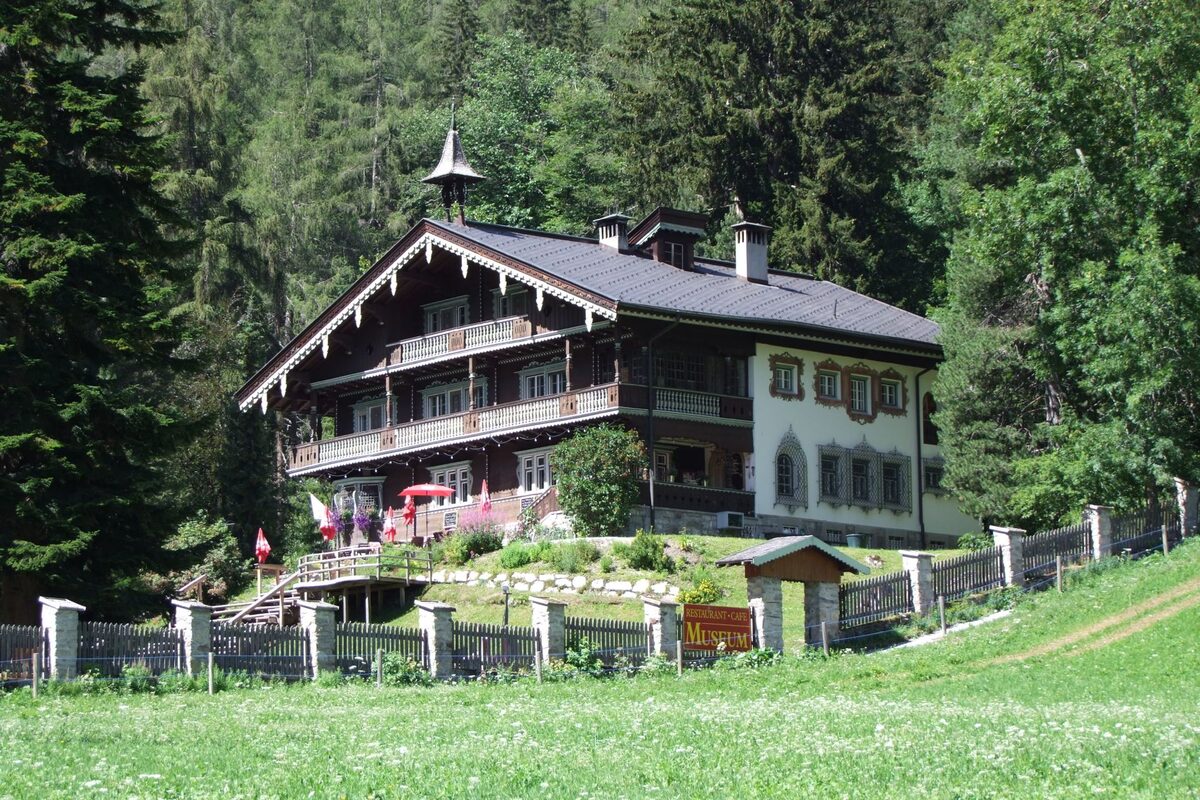 Villa Trier in summer, a timber chalet with a steep roof and balconies among the trees above St. Anton