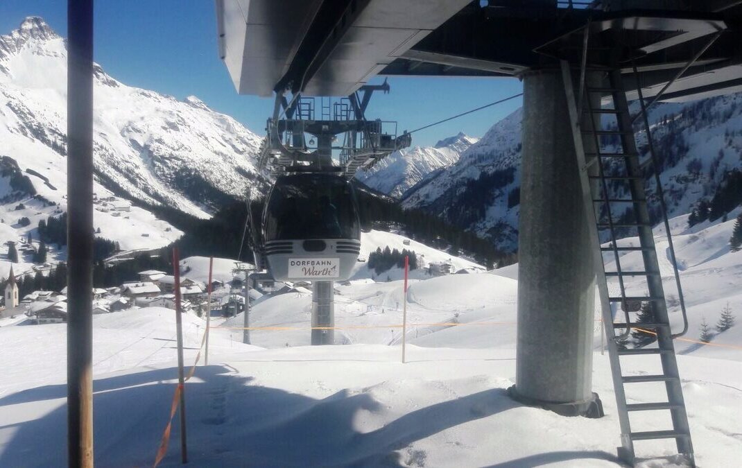 A Dorfbahn gondola cabin above the snowy slopes of Warth, with the village and its church below and a snowy peak behind