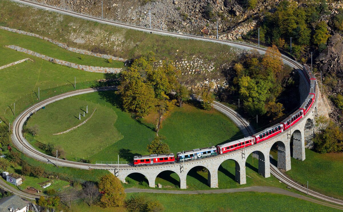 A red Bernina Express train crossing the nine-arched spiral viaduct at Brusio, seen from above
