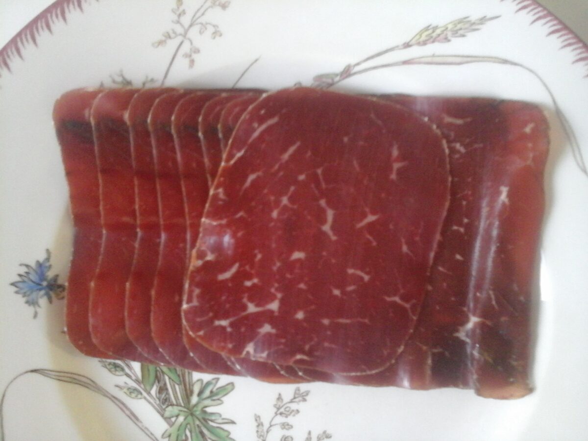 Thin slices of air-dried Bündnerfleisch stacked on a plate, the deep red beef marbled with fine fat
