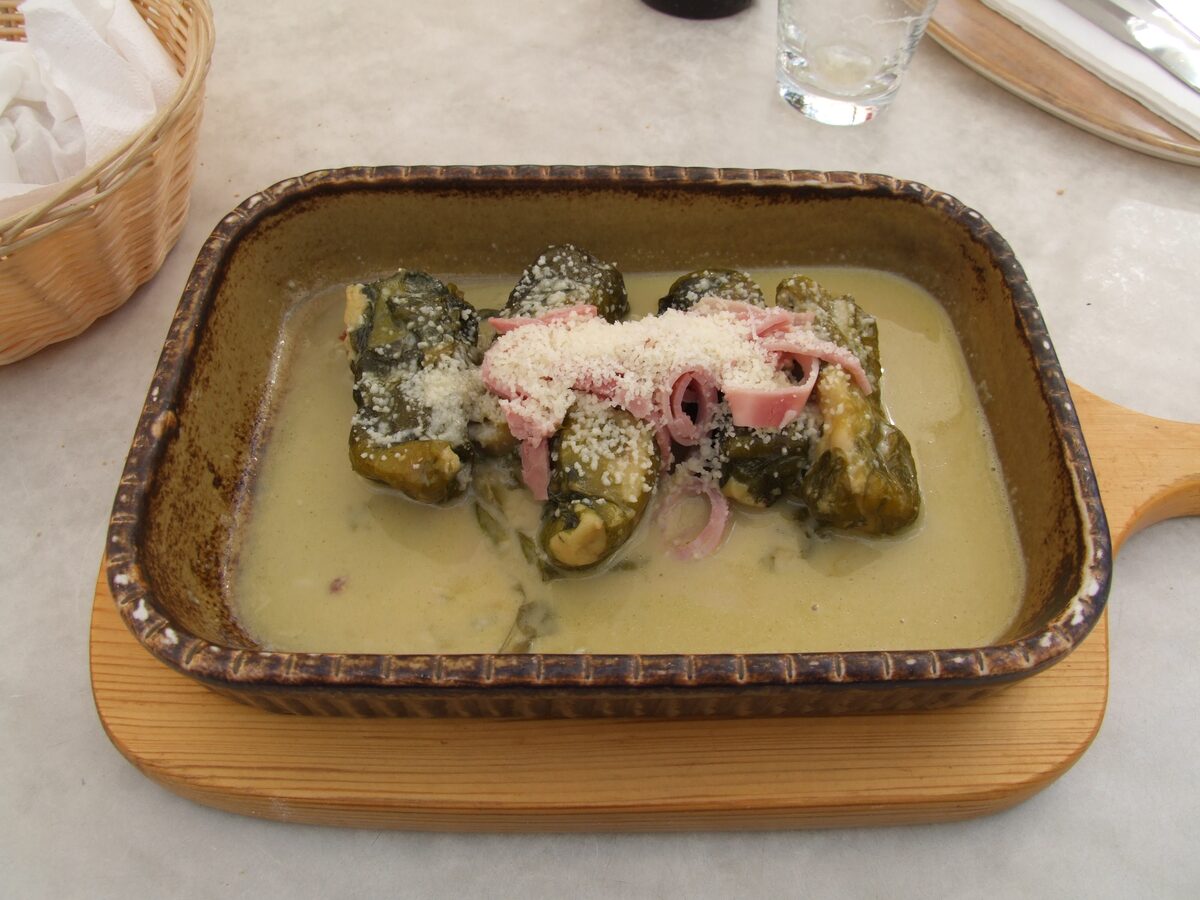 A baking dish of capuns, chard rolls in a creamy sauce topped with grated cheese and dried ham