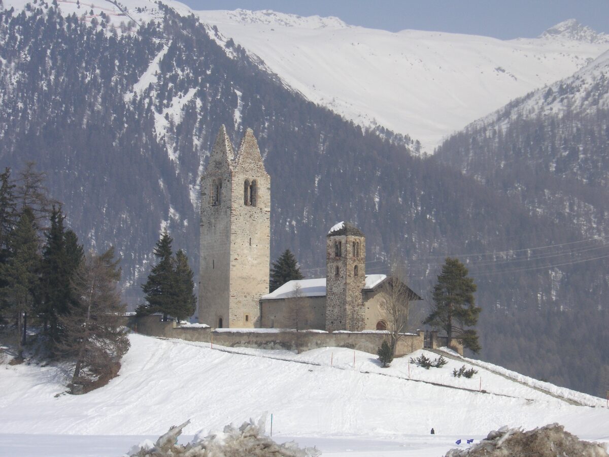 The tall bell tower and church of San Gian on its snowy hill above Celerina, with white mountain slopes behind