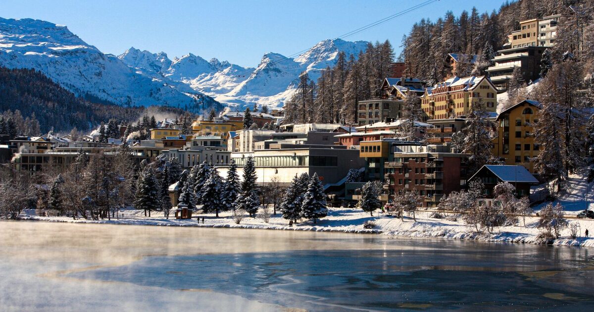 St. Moritz hotels and larch forest on the shore of the steaming, half-frozen lake, with snowy Engadin peaks behind