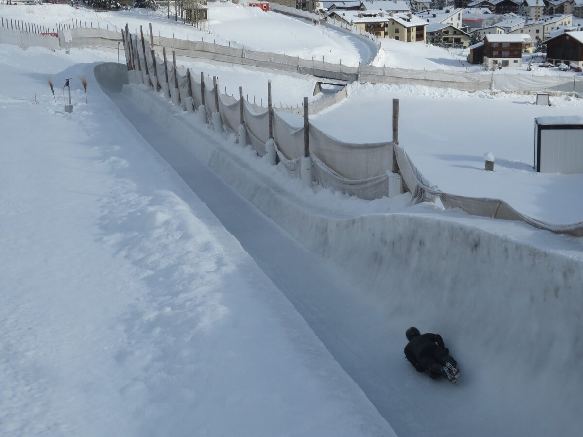The snow-banked Cresta Run track, with a rider on the course