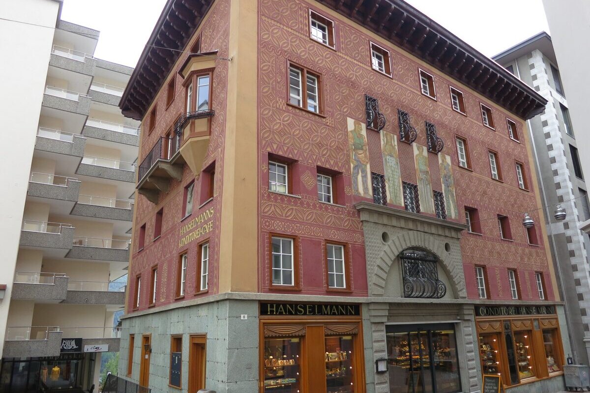 The painted red facade of the Hanselmann coffee house on Via Maistra, with shop windows at street level