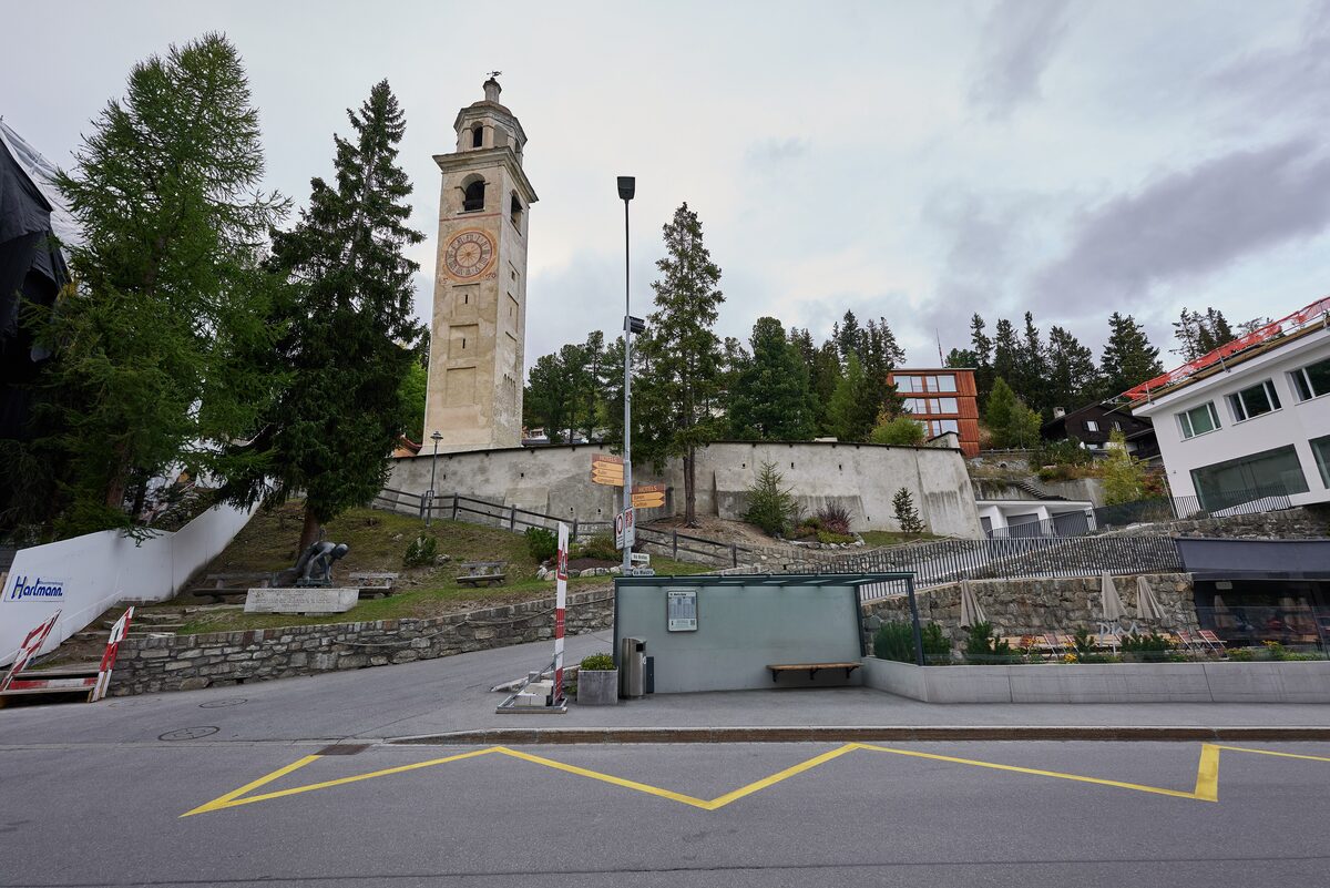 The medieval Leaning Tower of St. Moritz rising among larches above the street