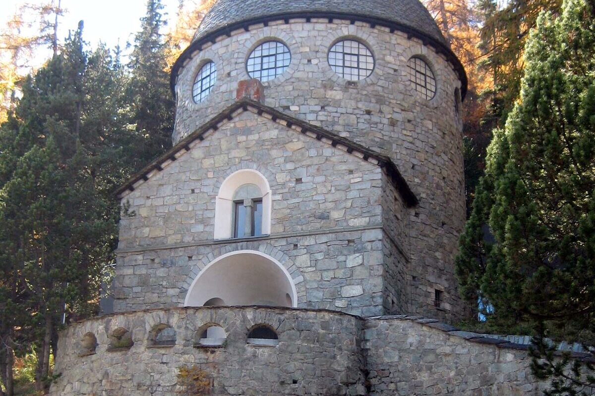 The domed stone tower of the Segantini Museum in St. Moritz, with round windows under a slate dome and larches behind