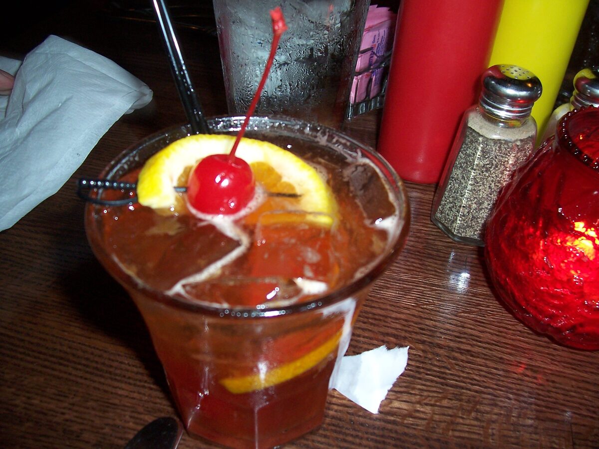 An Old Fashioned cocktail with an orange slice and cherry on a bar
