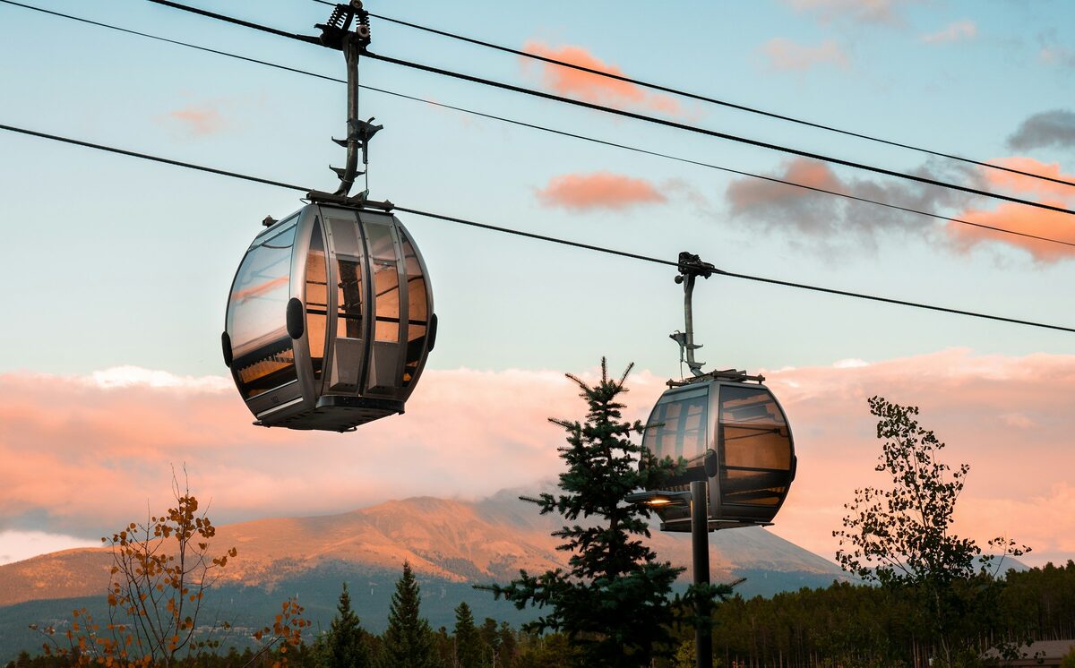Two gondola cabins hang from the cable above pine trees at sunset