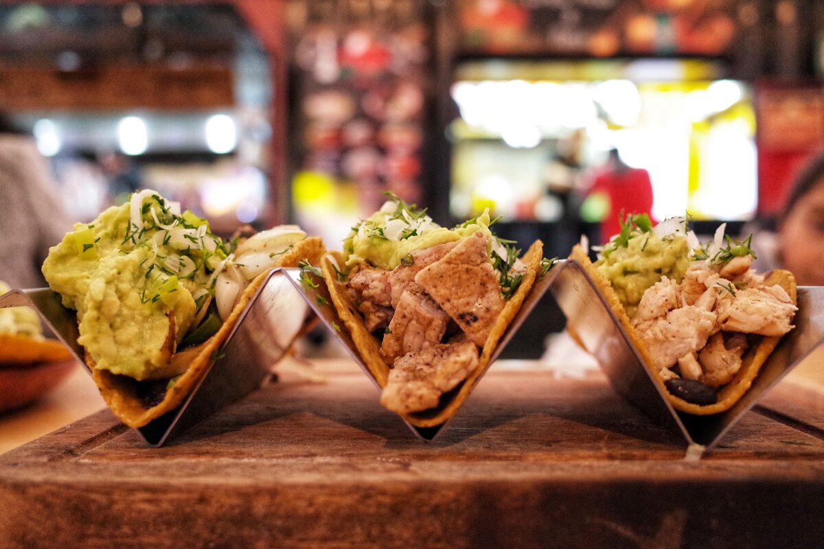 Three tacos in metal holders topped with guacamole and grilled chicken