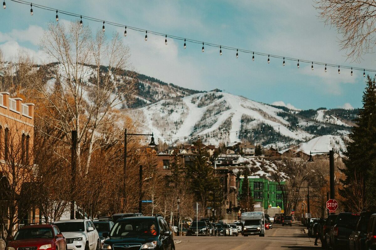 A downtown street with parked cars and snowy ski slopes rising behind
