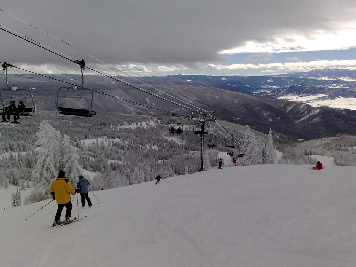 Skiers on a snowy run below a chairlift with frosted trees