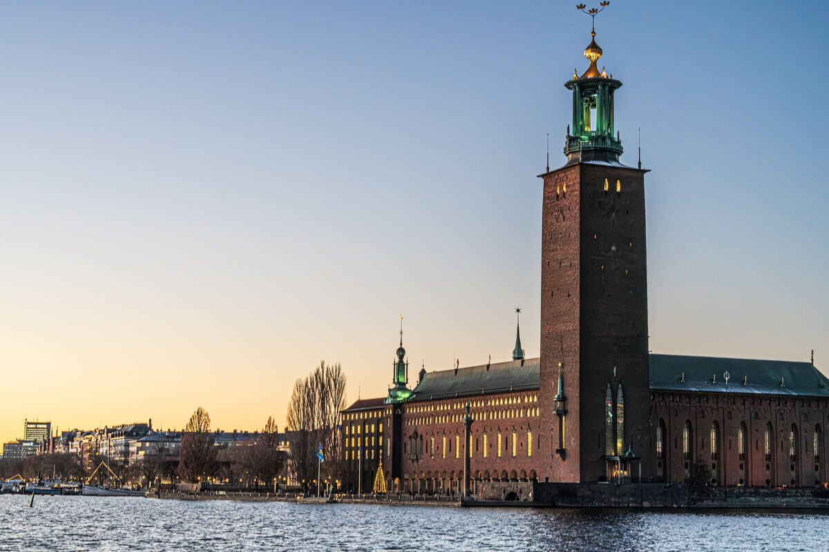 Stockholm City Hall with its tall brick tower and golden three crowns reflected in the water at sunset
