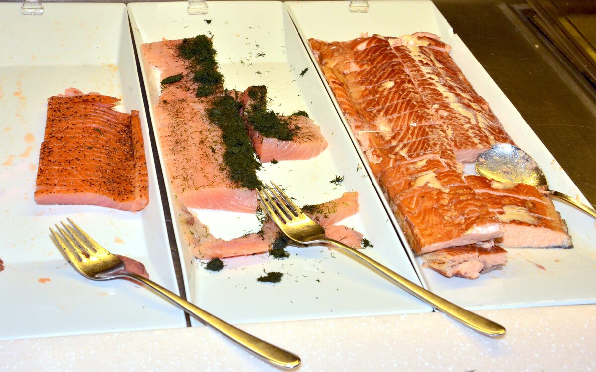 Trays of cured and smoked salmon on a buffet, one covered in chopped dill