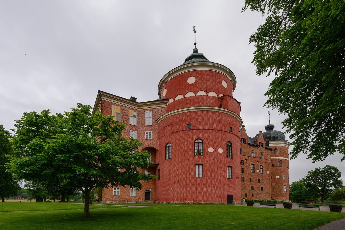 The round red-brick tower of Gripsholm Castle with green trees and a lawn in front